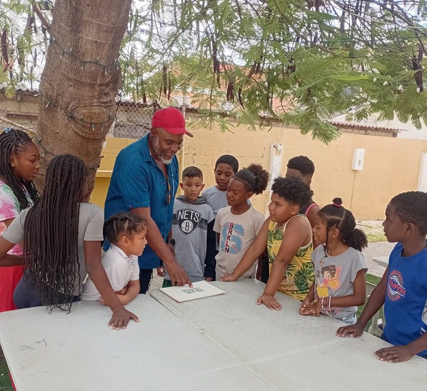 Children and supervisors around a table outside under a tree