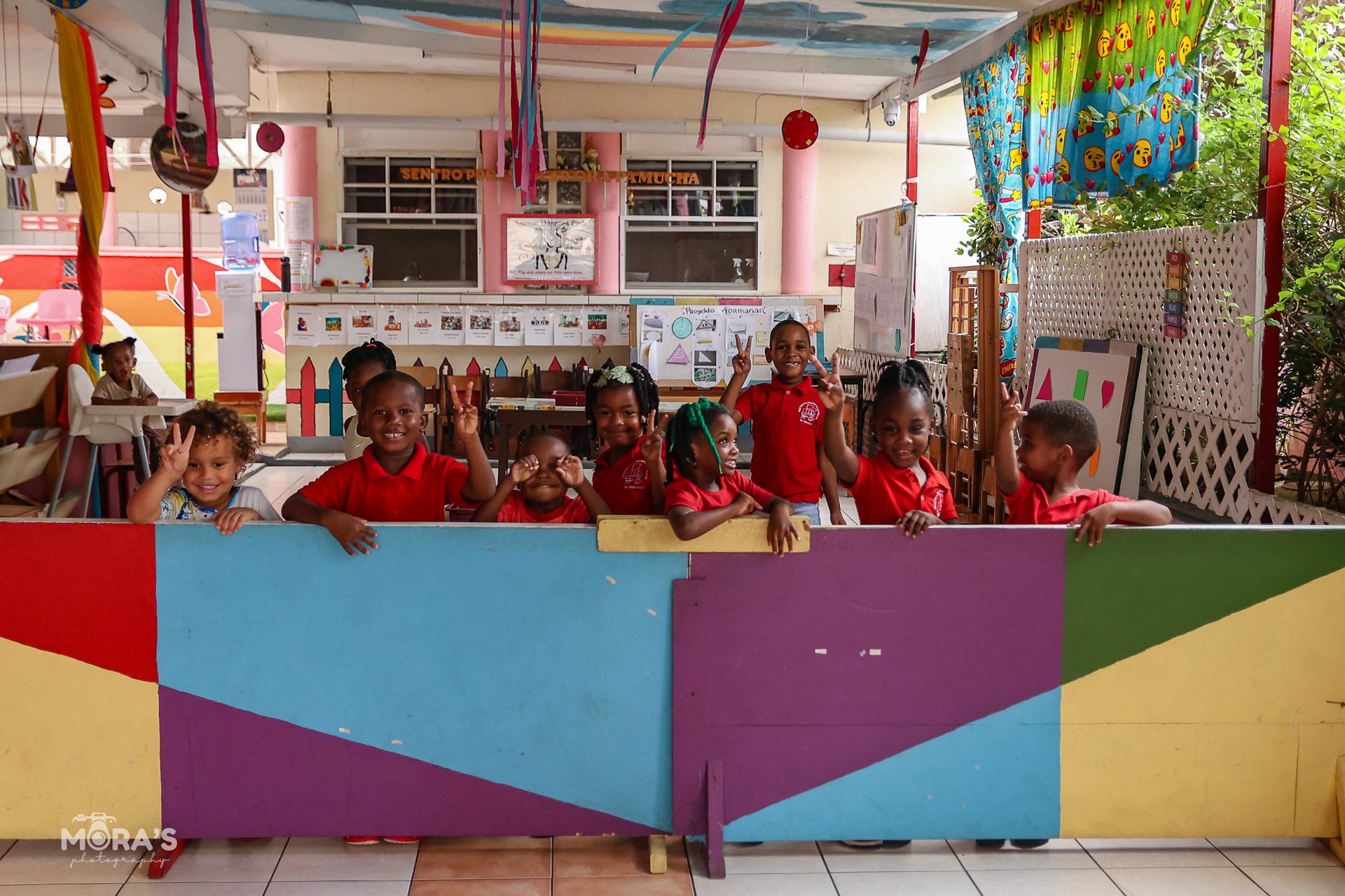 Children in red shirts behind a painted wall at school