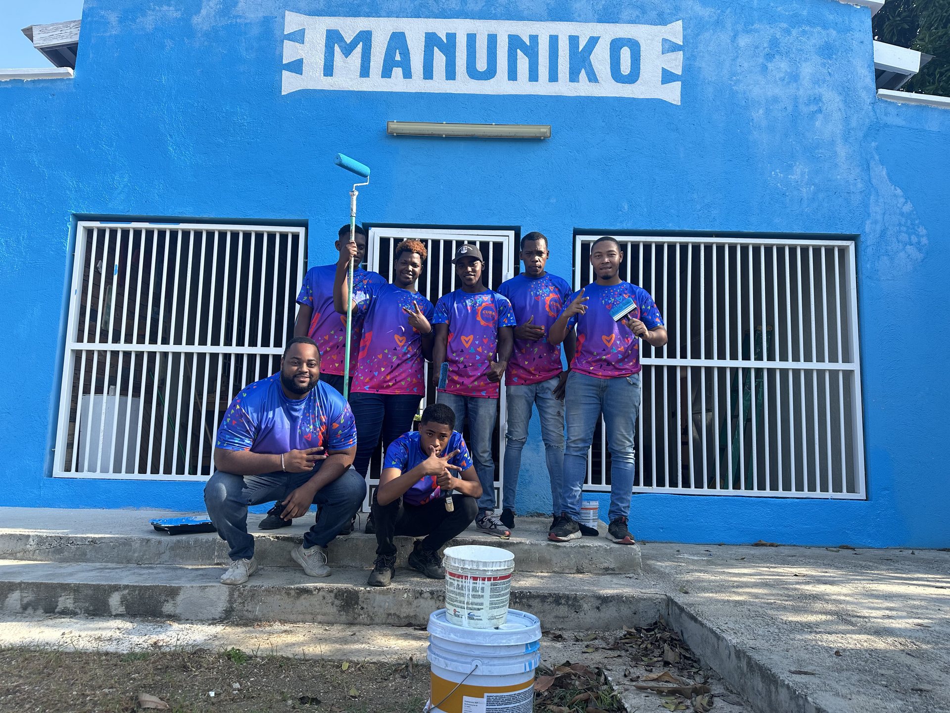 Medewerkers in paarse shirts voor het blauwe gebouw van Manuniko